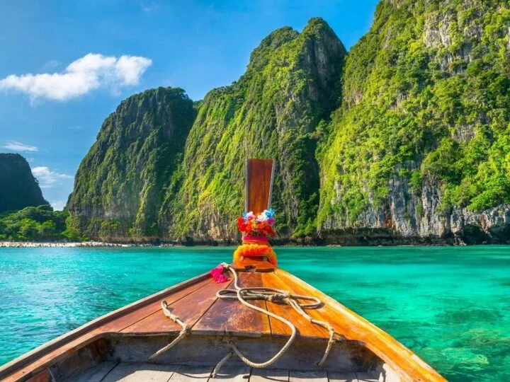 Longtailboot vor Kalksteinfelsen und türkisfarbenem Wasser in Thailand
